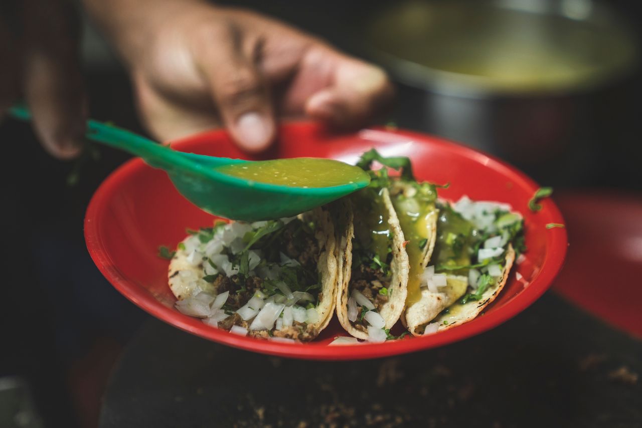 Close-up of delicious Mexican tacos being seasoned with green salsa.